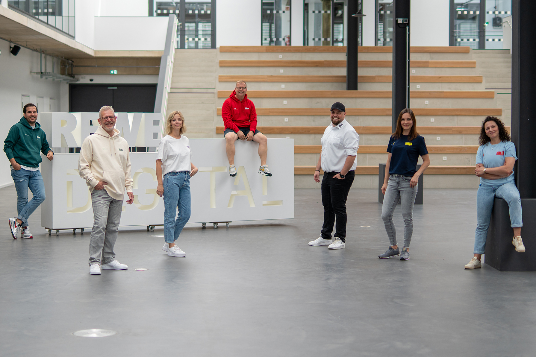 REWE digital team wearing merch in front of the REWE digital lettering in the atrium