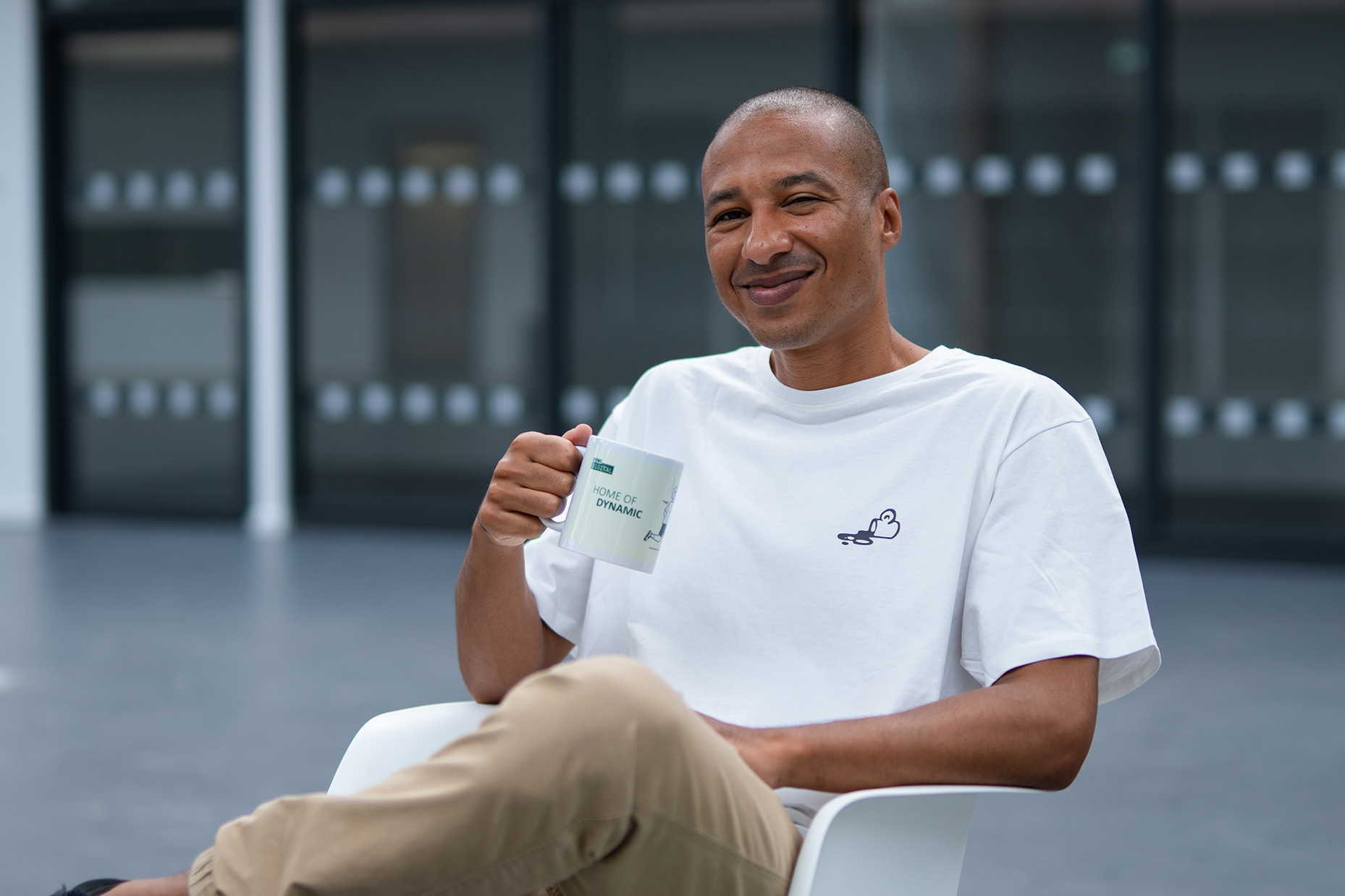 Colleague in a white REWE digital t-shirt holding a mug in the office